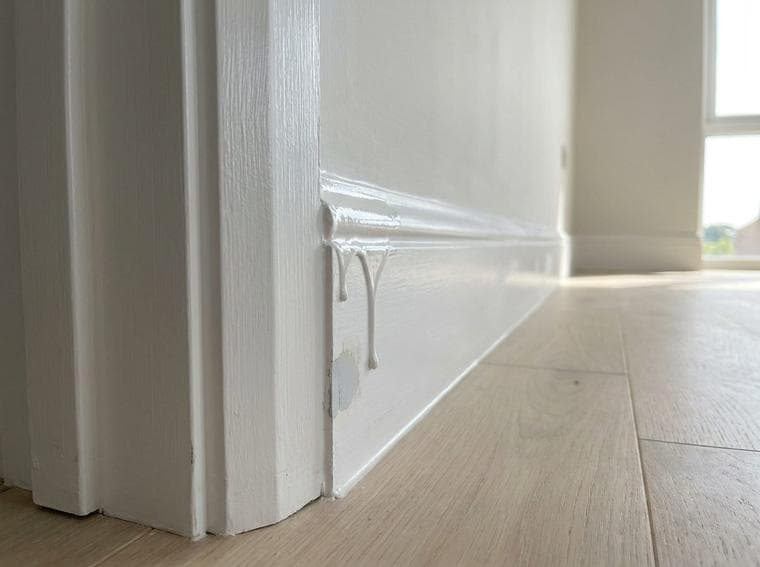Raised paint runs and drips remain on the baseboard beside the door casing.