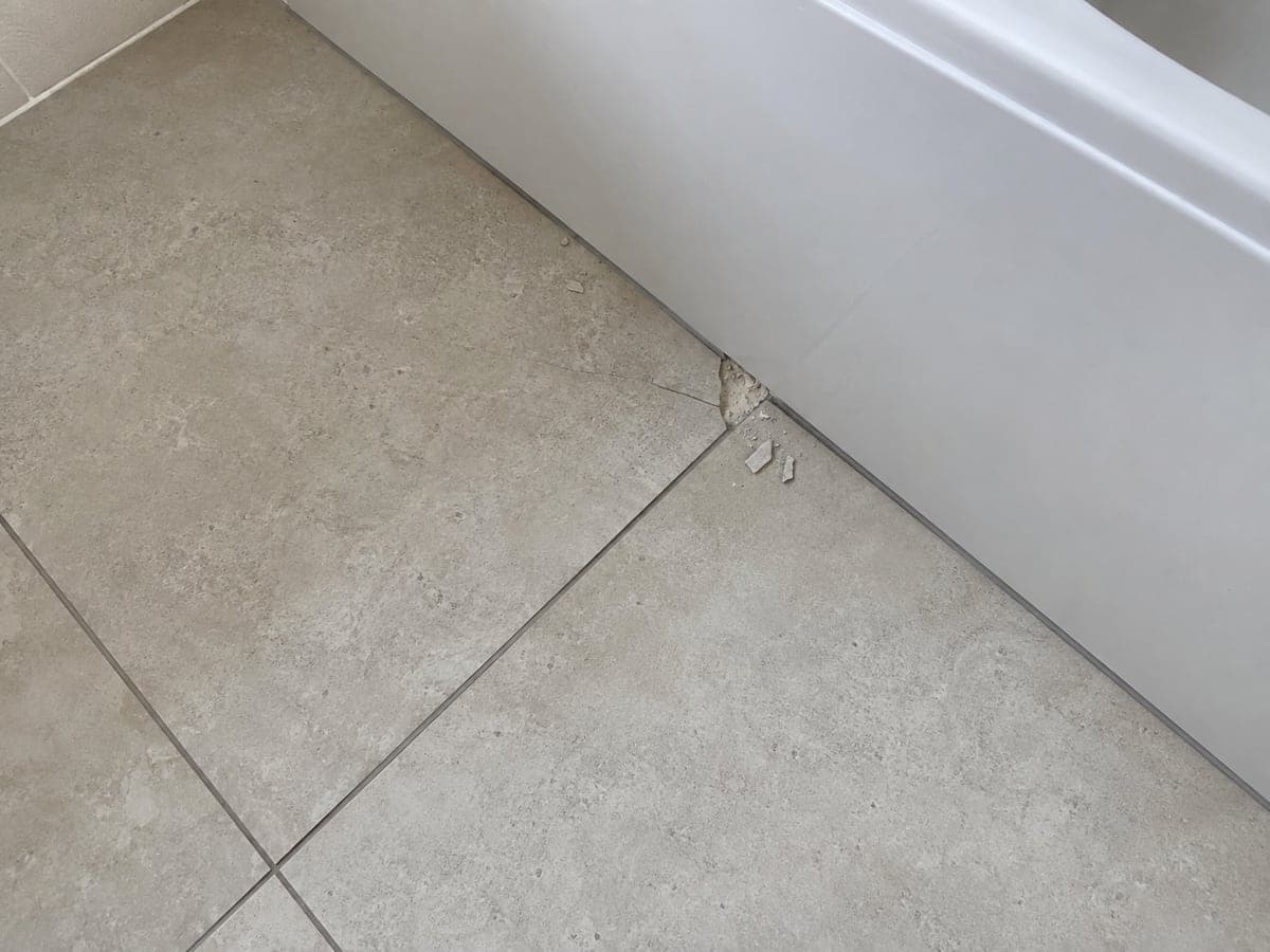 A floor tile is cracked and chipped, with a piece missing from the damaged edge.