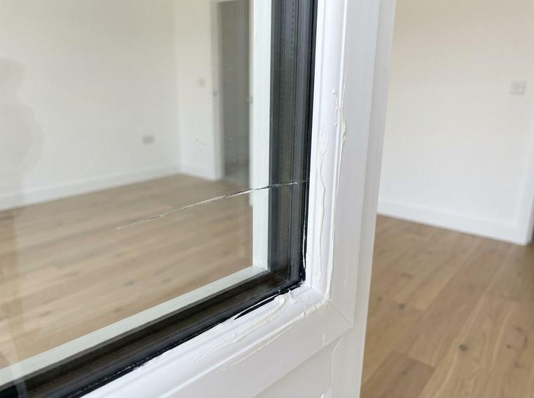 A scratch across the glass of a new insulated window in new construction, with dried sealant smeared on the white frame